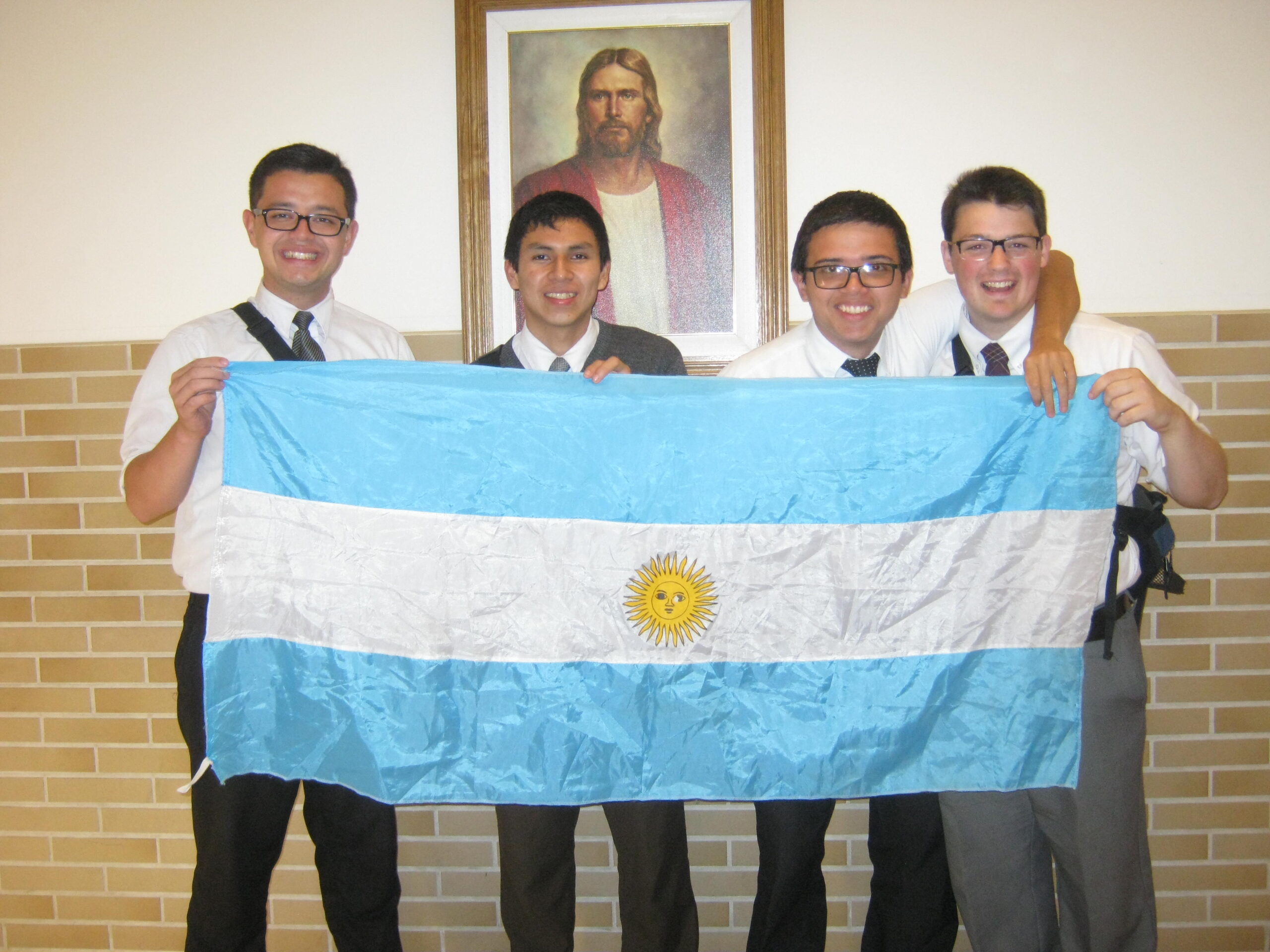 A group of LDS missionaries holding an argentina flag with a picture of jesus christ in the back.